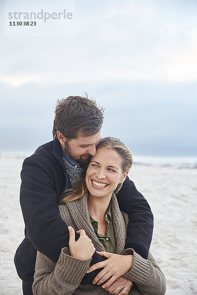 Lächelndes  zärtliches Paar  das sich am Winterstrand umarmt