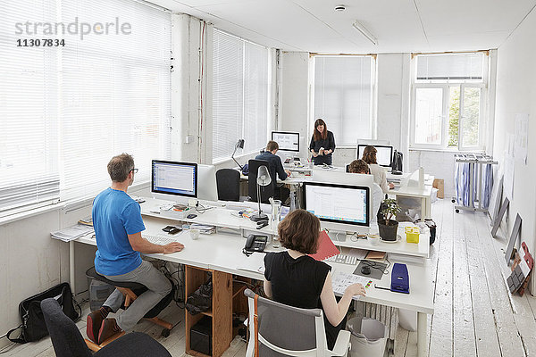 Ein modernes Büro  Arbeitsplätze für das Personal. Erhöhte Ansicht von sechs Personen  die an Schreibtischen sitzen. Ein Mann  der einen ergonomischen Kniestuhl benutzt.