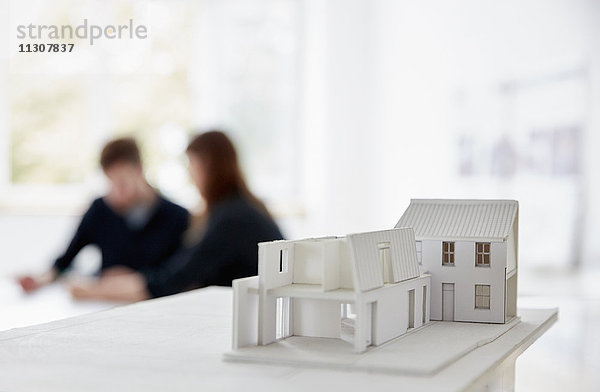 Architekturmodell eines Gebäudes mit zwei Personen bei einem Treffen  das im Hintergrund unscharf abgebildet ist. Kommunikation.