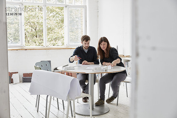 Ein modernes Büro. Zwei Personen bei einem Treffen  bei dem Pläne diskutiert werden. Architektonische Zeichnungen und Gebäudemodelle.