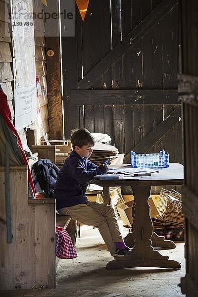 Ein Kind  das in einer Scheune an einem Tisch sitzt und seine Hausaufgaben macht.