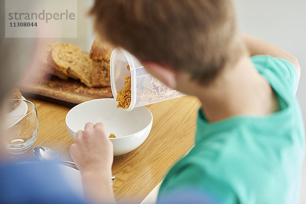 Das Frühstück. Ein Junge schüttet Müsli in eine Schüssel.