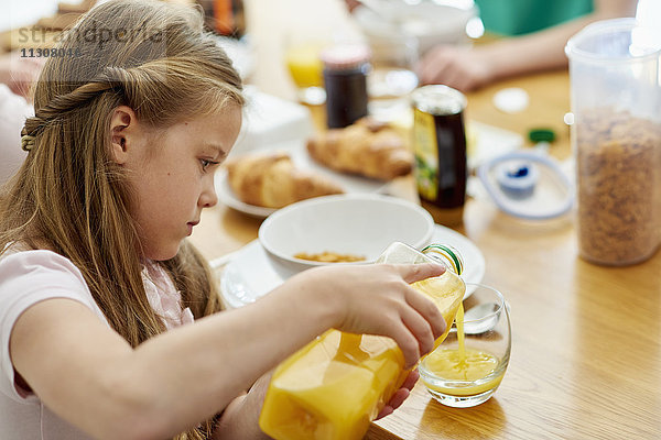 Eine Familie beim Frühstück. Ein Mädchen gießt Orangensaft in ein Glas.