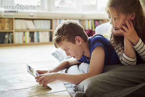 Zwei sitzende Kinder teilen sich ein digitales Tablett und schauen auf den Bildschirm.