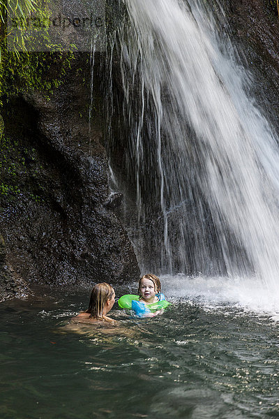 Mutter mit Tochter schwimmen unter Wasserfall