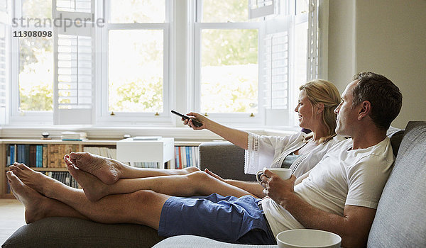 Ein Paar  Mann und Frau  die auf dem Sofa sitzen  gemeinsam fernsehen und die Fernbedienung halten.