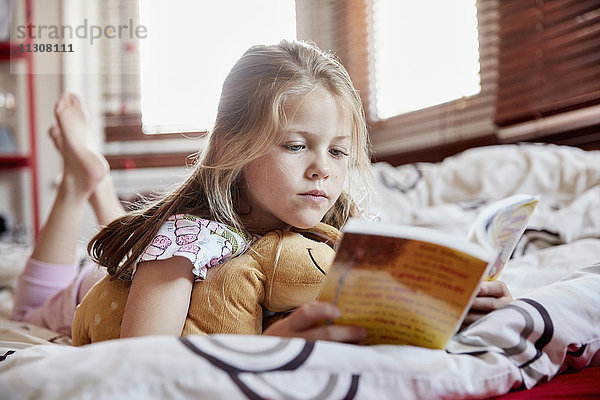 Ein Mädchen  das auf dem Bett auf der Vorderseite liegt und ein Buch liest.