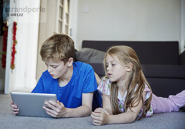 Zwei auf dem Bauch liegende Kinder teilen sich ein digitales Tablett und schauen auf den Bildschirm.