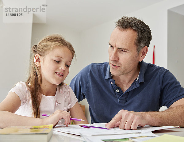 Ein junges Mädchen und ihr Vater sitzen  schauen sich ihre Schulbücher an und machen ihre Hausaufgaben.