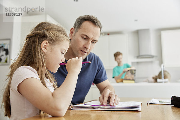 Ein junges Mädchen und ihr Vater sitzen  schauen sich ihre Schulbücher an und machen ihre Hausaufgaben.