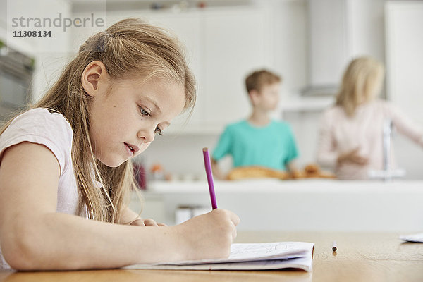 Ein Mädchen sitzt an einem Tisch in der Familienküche  hält einen Bleistift in der Hand und macht ihre Hausaufgaben.