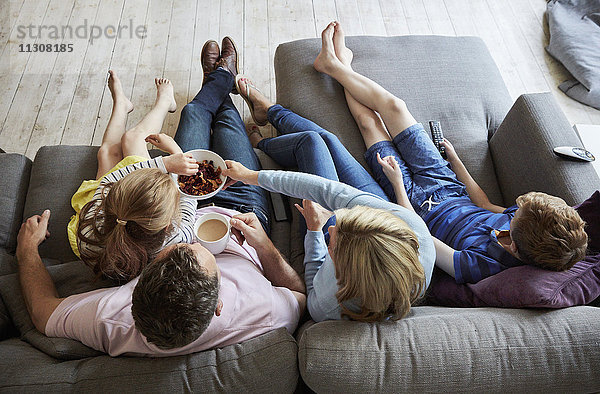 Eine Familie zu Hause. Blick von oben auf zwei Erwachsene und zwei Kinder  die gemeinsam auf einem Sofa sitzen.