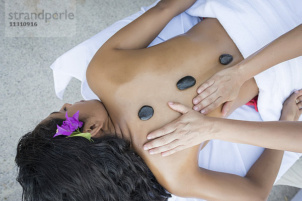 Junge Frau erhält eine Massage mit erhitzten Steinen auf dem Rücken