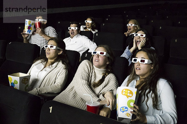 Erschrockene Leute mit 3D-Brillen  die einen Film in einem Kino sehen.