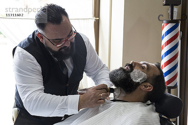 Barbier legt Rasierschaum in den Bart des Mannes