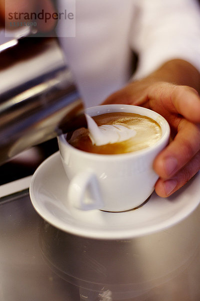 Milch von Hand in den Kaffee gießen
