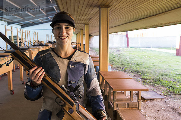 Porträt einer lächelnden Frau  die ihr Sportgewehr in einem Schießstand hält.