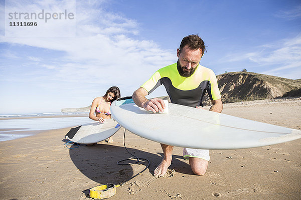 Ein Paar legt Paraffin auf seine Surfbretter am Strand.
