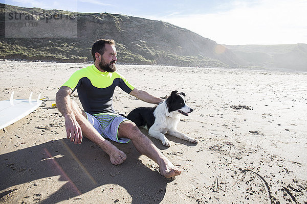 Mann mit Hund und Surfbrett am Strand