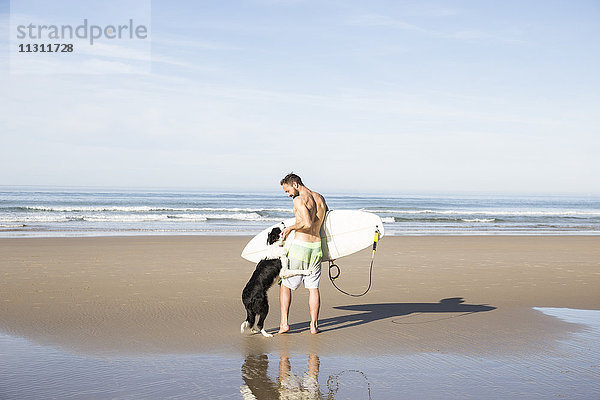 Mann mit Hund und Surfbrett am Strand