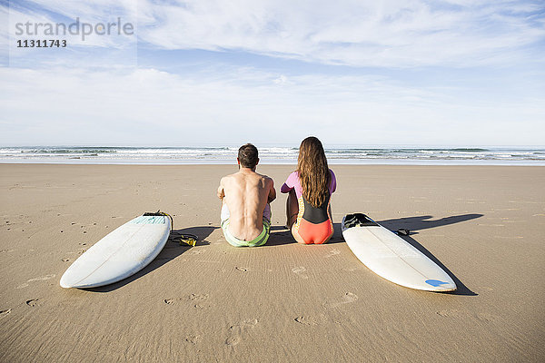 Paar mit Surfbrettern am Strand sitzend