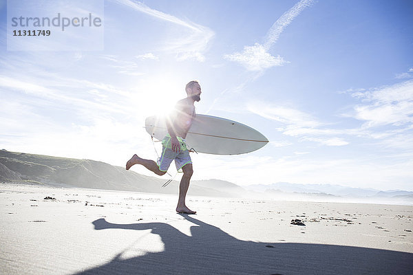 Mann mit Surfbrett am Strand unterwegs