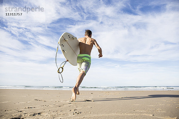 Mann mit Surfbrett am Strand unterwegs