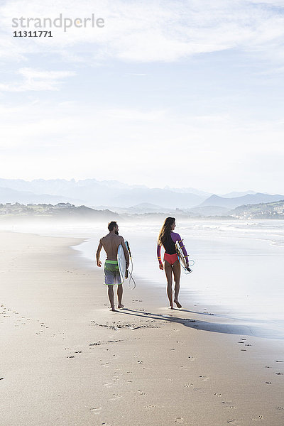 Paar mit Surfbrettern  die am Strand spazieren gehen