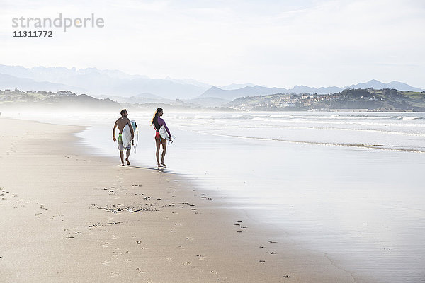 Paar mit Surfbrettern  die am Strand spazieren gehen