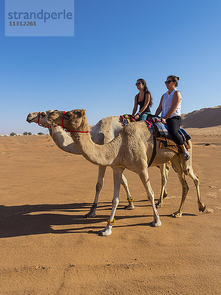 Oman  Al Raka  Rimal Al Wahiba Wüste  zwei Frauen reiten auf Dromedaren