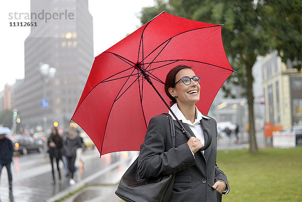 Deutschland  Berlin  glückliche Geschäftsfrau mit rotem Schirm am Potsdamer Platz
