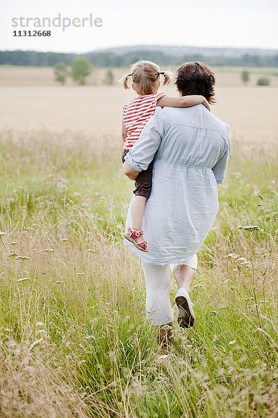 Mutter trägt Tochter beim Spaziergang auf einer Wiese