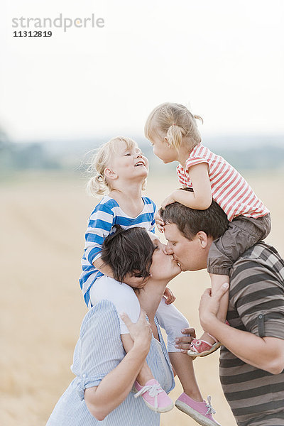 Familie mit zwei Kindern  die sich auf einem Feld küssen