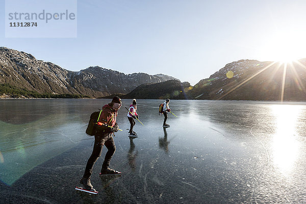 Freunde beim Schlittschuhlaufen auf einem zugefrorenen See bei Sonnenuntergang