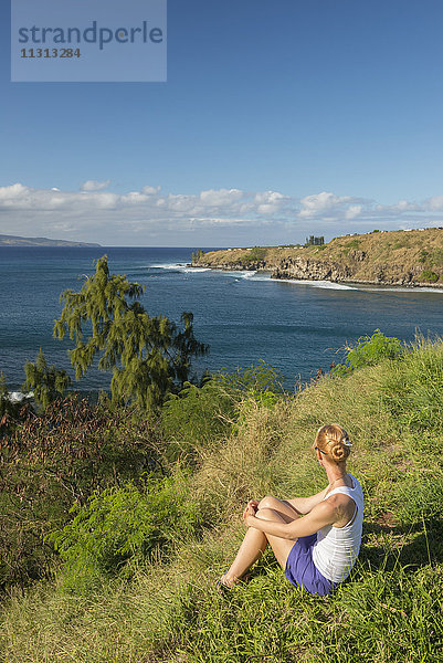 USA  Vereinigte Staaten  Amerika  Hawaii  Maui  Kaanapali  Küste bei Kapalua  Mädchen sitzt im Gras mit Blick auf die Bucht MR