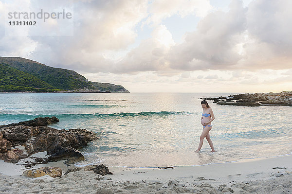 Eine schwangere Frau  die am Strand spazieren geht.