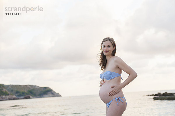 Lächelnde schwangere Frau am Strand stehend