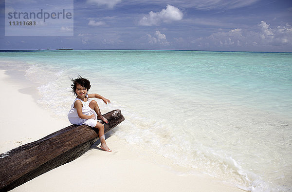 Malediven  Mädchen auf einem Baumstamm am Strand sitzend