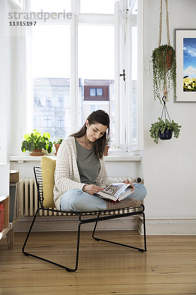Frau zu Hause sitzend auf Stuhl Lesebuch