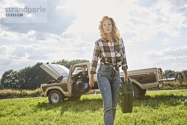 Frau geht mit Benzinkanister auf dem Feld neben dem Pick-Up Truck