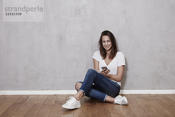 Lächelnde junge Frau auf dem Boden sitzend mit Handy