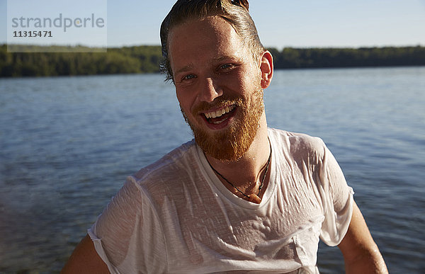 Glücklicher junger Mann mit nassem T-Shirt am See