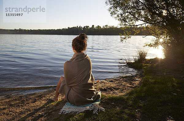 Junge Frau bei Sonnenuntergang am See sitzend