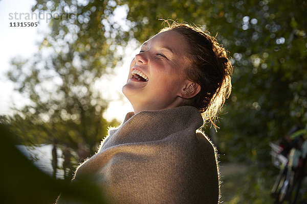 Lachende junge Frau in eine Decke gewickelt bei Sonnenuntergang