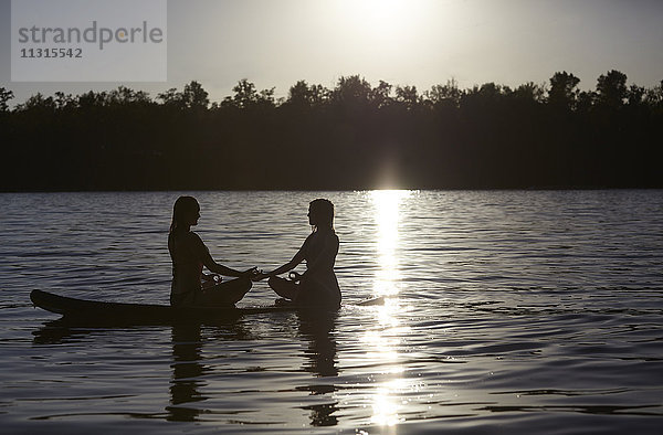 Zwei Frauen beim Yoga auf dem Paddelbrett bei Sonnenuntergang