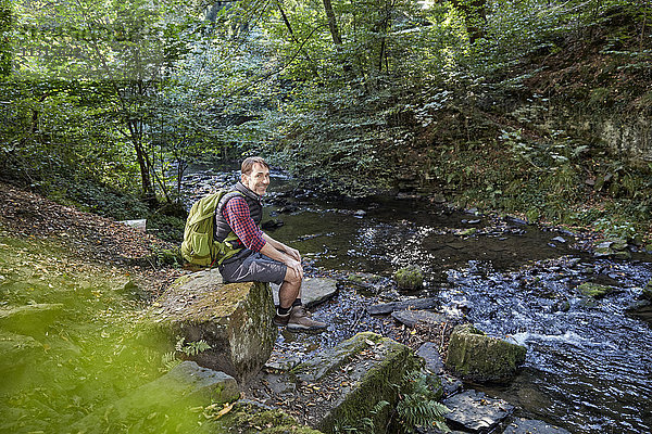 Wanderer im Wald auf Felsen am Bach sitzend
