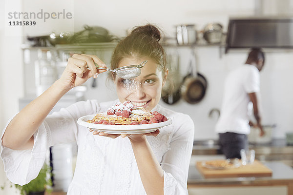 Porträt einer jungen Frau  die in der Küche Puderzucker auf Waffeln streut.