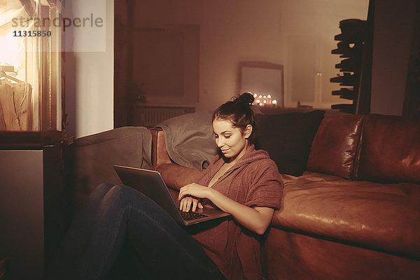 Junge Frau entspannt mit Laptop im beleuchteten Wohnzimmer