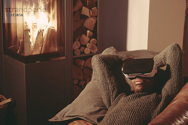 Junger Mann mit Virtual Reality Brille auf der Couch zu Hause liegend