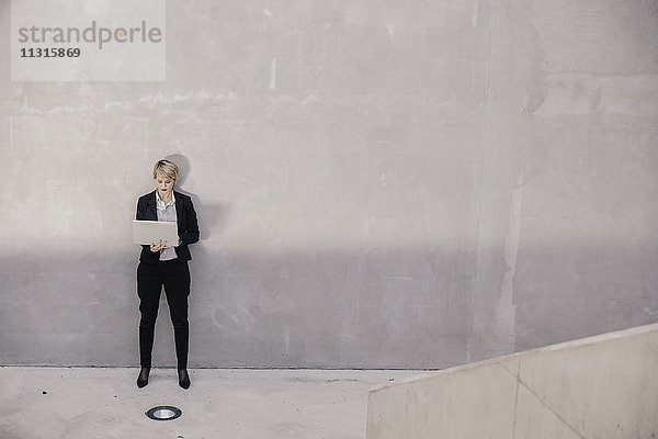 Geschäftsfrau vor der Betonwand stehend mit Laptop